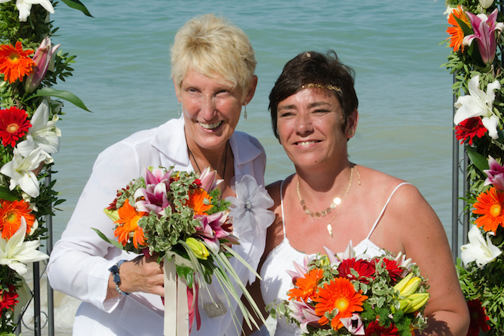 Happy gay couple pose on a beach after their wedding ceremony