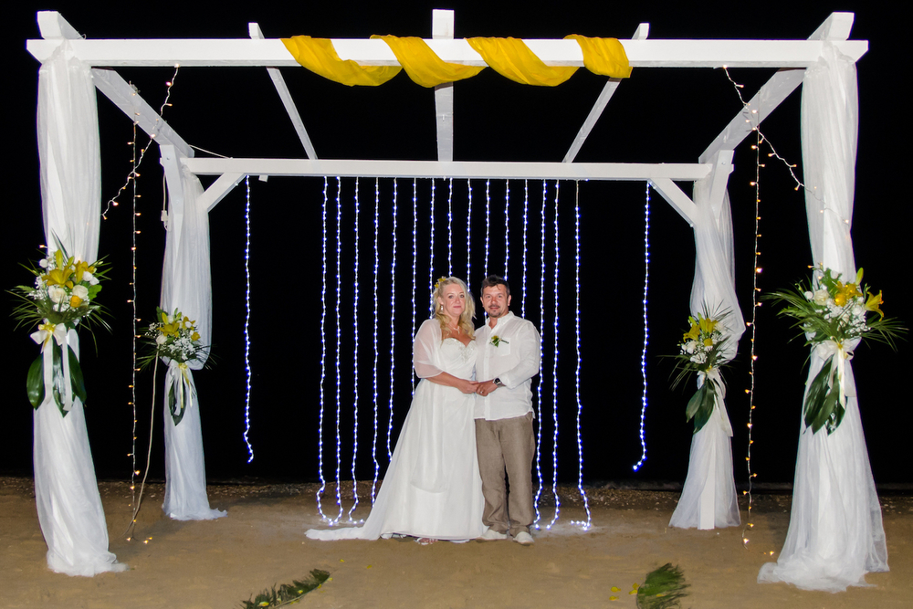 Sam and Steve on a beach under a wedding ceremony arch