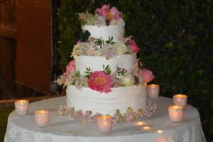 a large three layer, iced wedding cake decorated with flowers sitting on a table decorated with candles.
