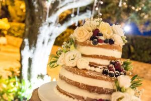 Italian wedding cake decorated with flowers on a table under an olive tree.