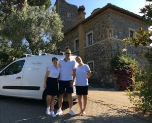 3 wedding planners in Italy posing in front of their van with a castle wedding venue in the background.