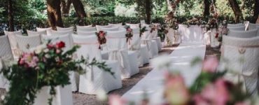 wedding ceremony with white covered chairs and coloured flowers in dappled sunshine under trees