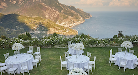 wedding dining tables set up on a terrace with a view of the Amalfi coast behind