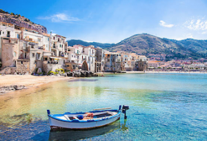 small wooden boat tied up to a beach in front of a Sicilian village 