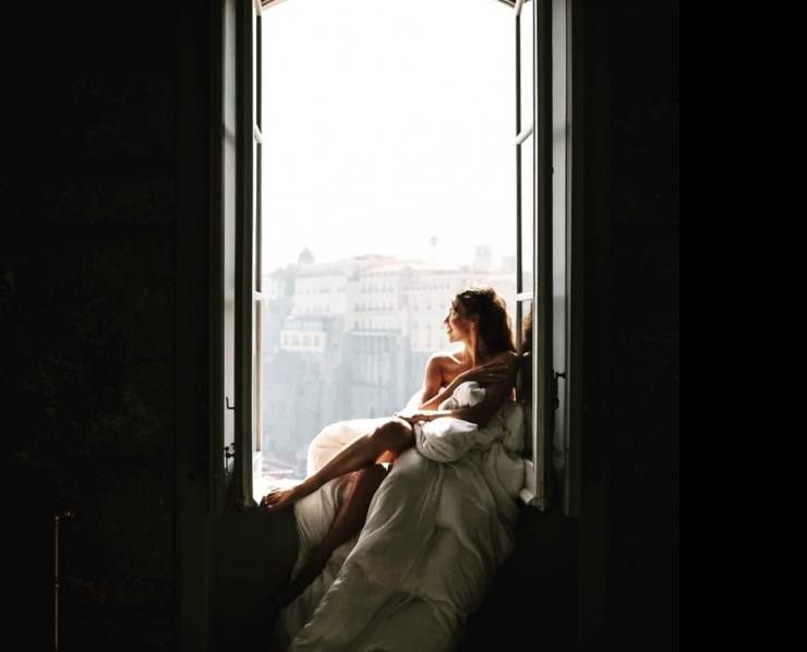 Relaxed bride at destination wedding in Italy looks out of antique window.