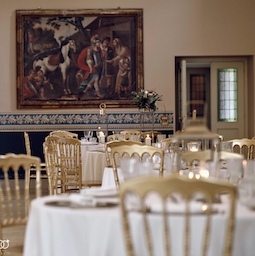 Elegant dining room set up for an Italian wedding banquet with gold chairs and white tablecloths.