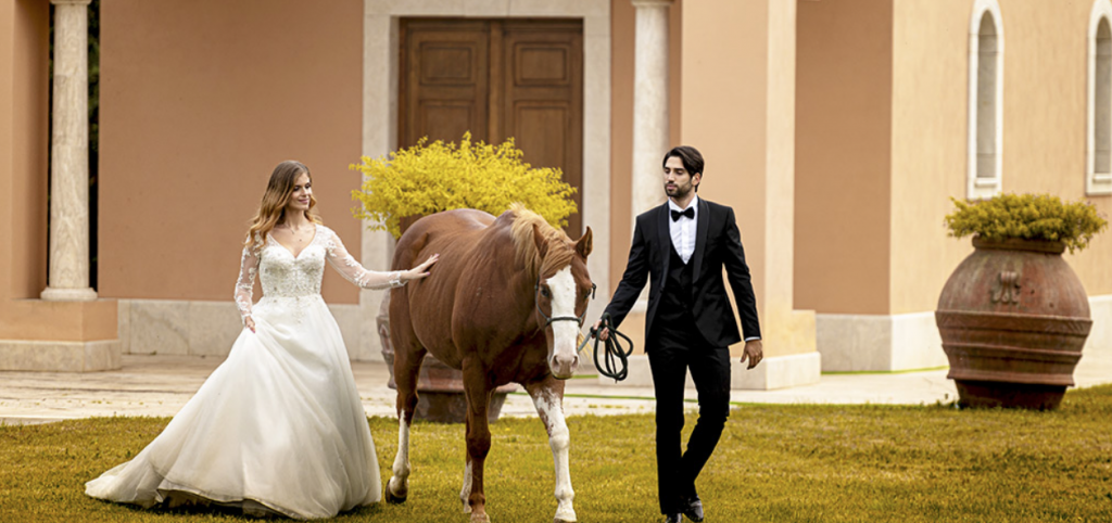 Elegant couple lead a horse across a lawn at a wedding venue in Rome.